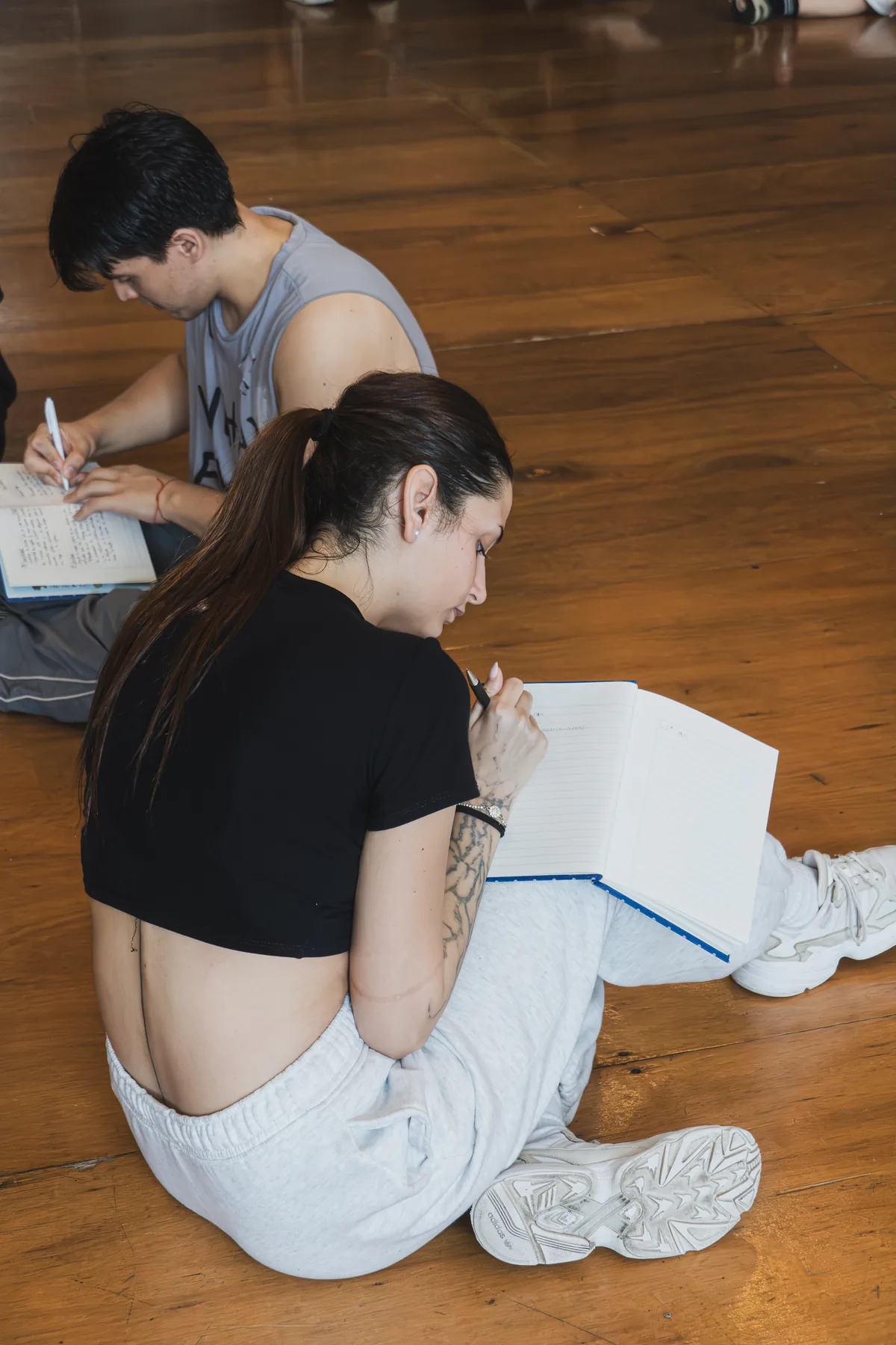 Dos estudiantes escribiendo en sus cuadernos en el suelo